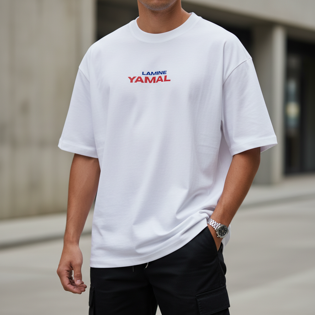 A white oversized short-sleeve t-shirt hanging on a wooden hanger, featuring 'LAMINE YAMAL' printed on the chest in blue and red.